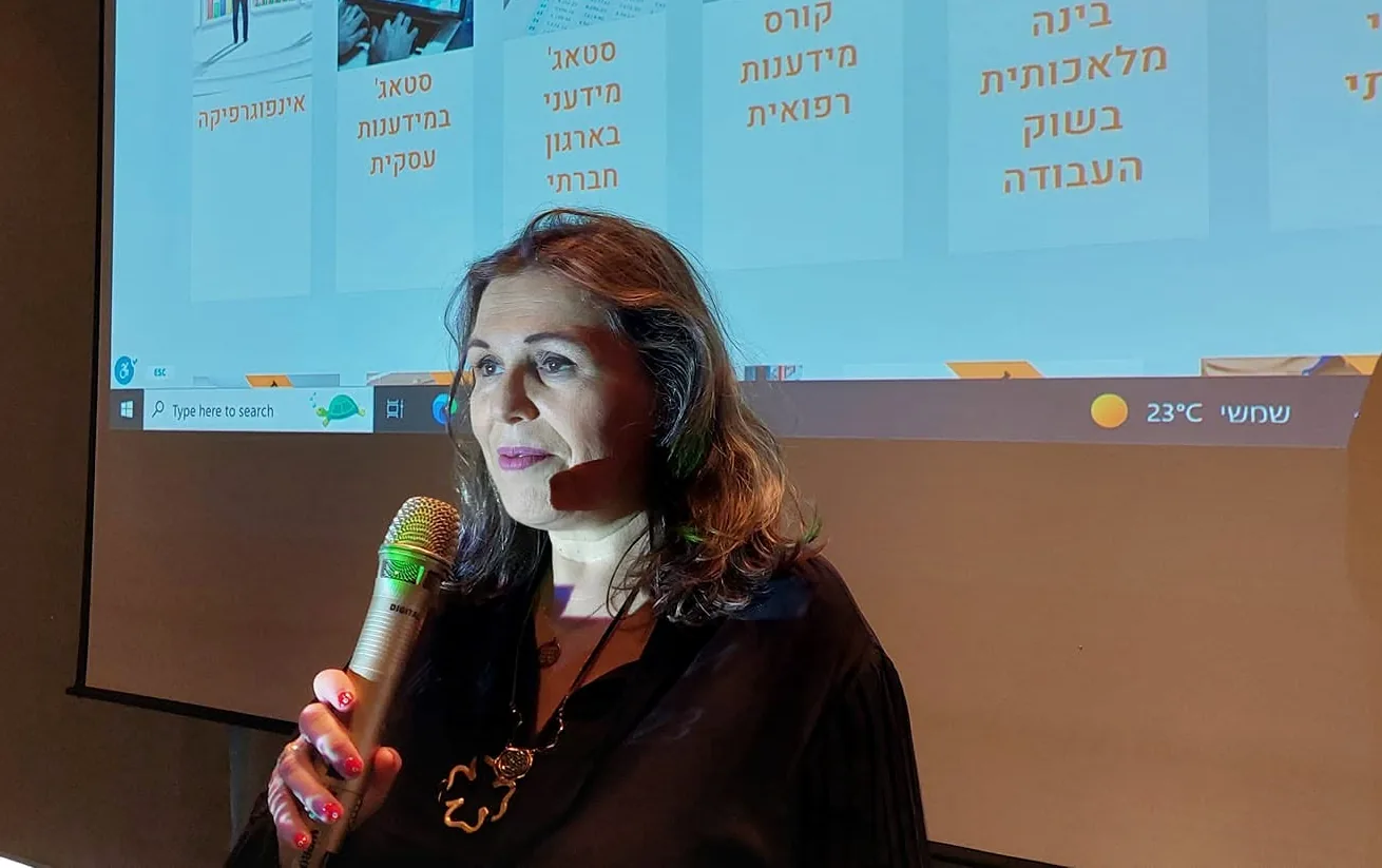 ד״ר ענת קלומל-פרוכצוייג מדברת למיקרופון וברקע שקופית על תחומי לימוד