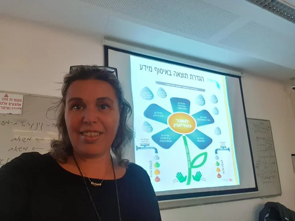 ד״ר ענת קלומל-פרוכצוייג לצד מצגת של מודל פרח